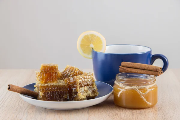 Pedaços de mel dourado pente em uma mesa com chá, limão e cinna — Fotografia de Stock