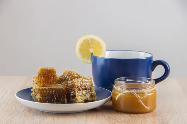 Trozos de peine de miel dorada sobre una mesa con té, limón y cinna —  Fotos de Stock