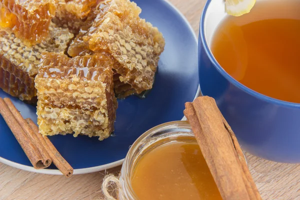 Trozos de peine de miel dorada sobre una mesa con té, limón y cinna —  Fotos de Stock