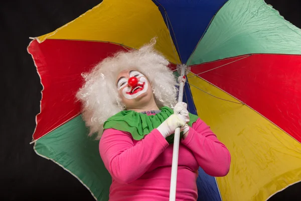 Jolly good funny clown with a multi-colored umbrella on a black — Stock Photo, Image