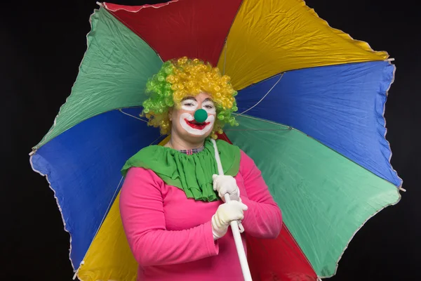 Jolly good funny clown with a multi-colored umbrella on a black — Stock Photo, Image