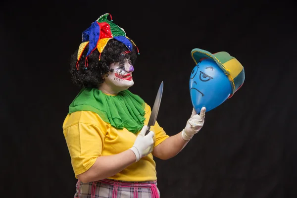 Angry ugly clown wants to kill a balloon in the cap — Stock Photo, Image