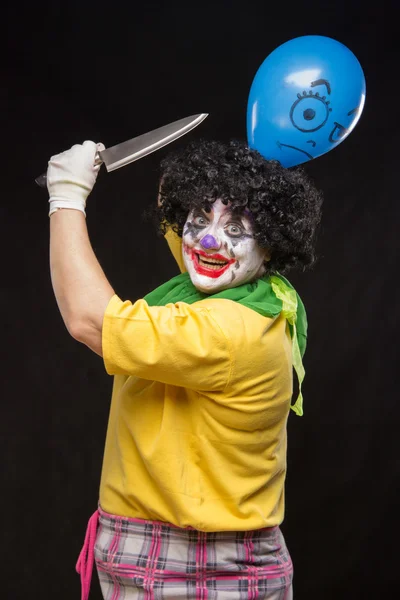 Angry ugly clown wants to kill a balloon in the cap — Stock Photo, Image