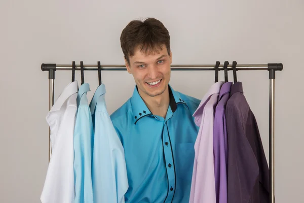 Молодой сексуальный мужчина выбирает рубашку из различных рубашек висит — стоковое фото