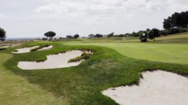 Güneşli bir günde Portekiz 'de bir golf kulübünün hava manzarası. Arka planda yeşil bir golf sahası, tek bir golfçü ve okyanus manzarası var..