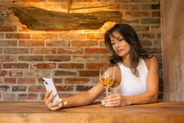 Sade ve sade bir iç mekanda zarif bir kadın şarabını yudumlarken telefonuyla anın tadını çıkarıyor.