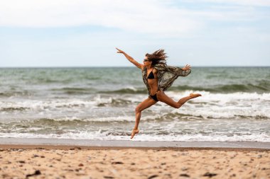 Bir kadın sevinçle güzel kumlu sahilde koşar, dalgaları kucaklar ve kaygısız ruhunu
