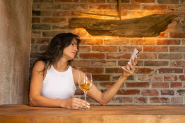 Rahat ve rahat bir köy ortamında, bir kadın şarabını yudumlarken ve akıllı telefonunu kullanırken rahatlamayı sever.