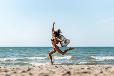 Enerjik deniz kenarı egzersizi, coşkulu bir kadın okyanus spreyi ve esintisiyle kıyı kumlarında enerjik bir egzersiz yapıyor.