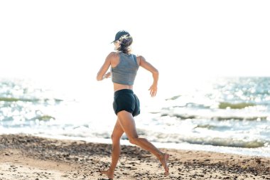 Kadın uzak ufuk çizgisine doğru dizginsiz hareket eder, kadın dışarıya doğru giden ışıl ışıl kıyı şeridi boyunca özgürce egzersiz yapar.