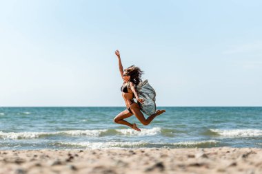Neşeli hareketli güneşli sahil, sıcak sahil boyunca koşan neşeli kadın, güneşli kumlu sahil şeridinde dans eden enerjik kadın