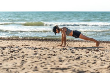 Sahilde tahta döşeme yapan bir kadın, sahilin kenarında antrenör, dayanıklılık ve dengeyi göstermek için kalas sallıyor.