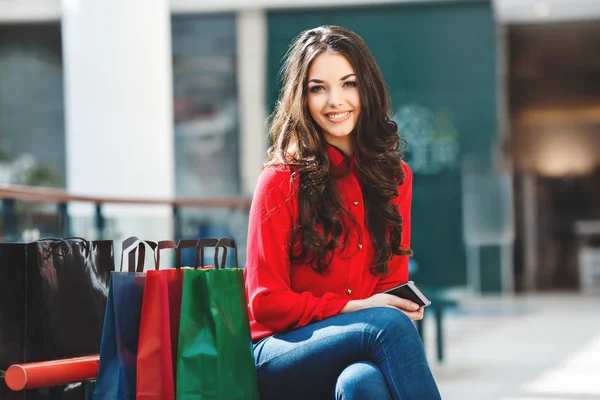 Sorrindo menina sentada no shopping com sacos de compras e telefone — Fotografia de Stock