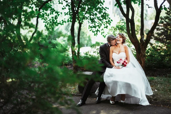 Bruid en bruidegom zittend op een bankje in het park — Stockfoto