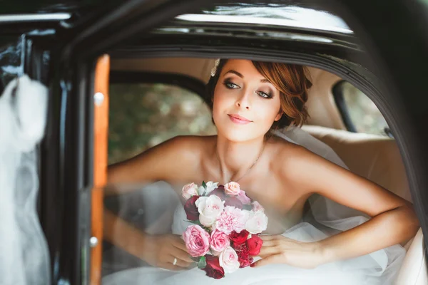 Bride sitting in wedding car and looking at window — Stock Photo, Image