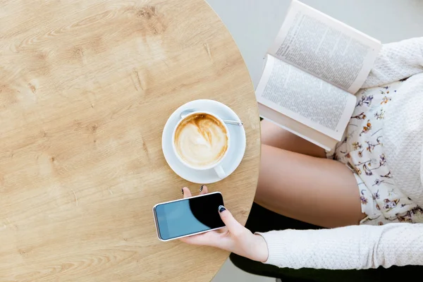 Patas de niña, taza de café, libro y teléfono móvil — Foto de Stock