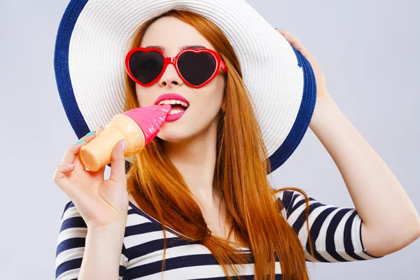 Девушка в шляпе и солнцезащитных очках кусает мороженое — стоковое фото