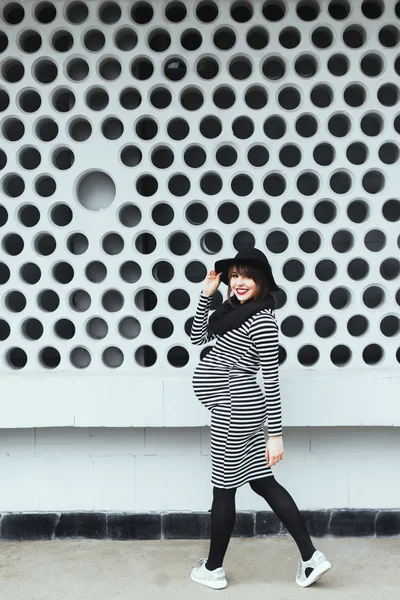 스트라이프 드레스와 검은 모자 벽 근처에 임신한 여자 — 스톡 사진