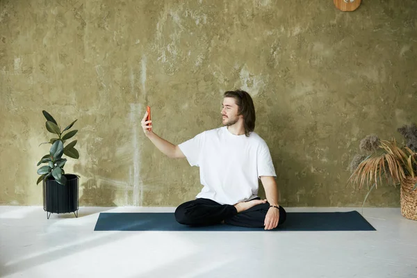 man sitting in lotus yoga pose using phone, meditation lesson online with professional mental teacher, copy space