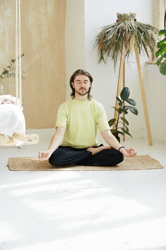 peacefull man in lotus pose and yoga mudra at home, young mindfull guy meditating on the floor