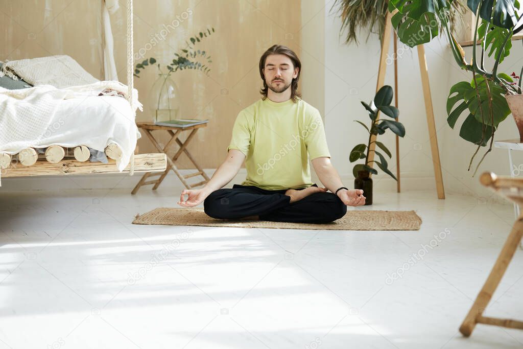 handsome man with long hair meditaing in lotus pose, beaautiful person learning mindfulness at home
