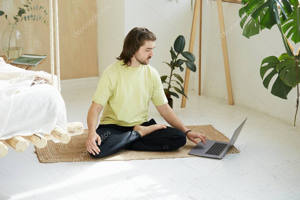 lovely person in yoga asana using laptop, yoga teacher sitting in pose on the floor and typing on computer, online studying of mindfullness