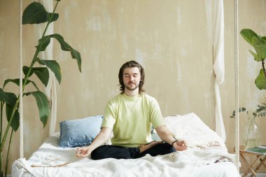 Yatakta oturup meditasyon yapan sakin bir adam, zihinsel sağlık konsepti ve meditasyon teknisyeniyle yaşayan bir uyum.