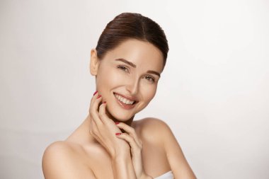 Kameraya gülümseyen sevimli bir kadın, parlak makyajlı ve parlak dudaklı muhteşem bir kadın, beyaz tenli yüzüne dokunuyor.