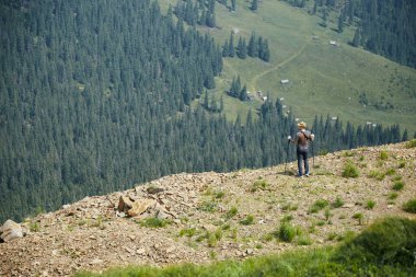 Dağ ve orman manzaralı kayanın tepesinde duran adam olağanüstü manzara sırt çantalı yeşil dağlar.