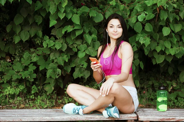 Chica atractiva de fitness, con auriculares, sosteniendo su teléfono inteligente —  Fotos de Stock