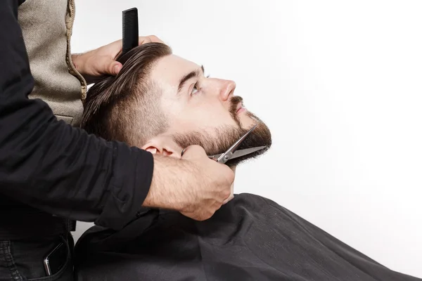 Парикмахер стрижет бороду человека в студии — стоковое фото