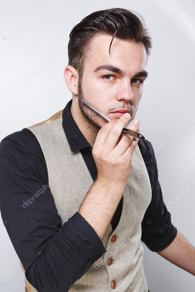 Young barber holding razor near his face