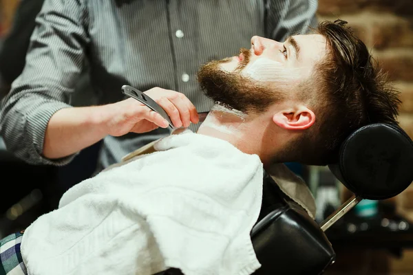 Парикмахер стрижет бородатого парня — стоковое фото