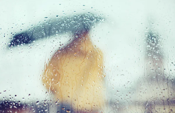 Man with umbrella through wet glass