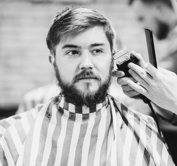 Парикмахер стрижет бородатого парня — стоковое фото