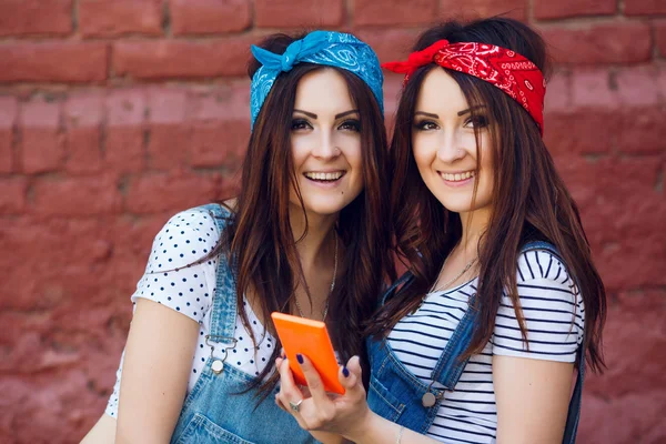 Zwillinge Mädchen mit orangefarbenem Smartphone. — Stockfoto