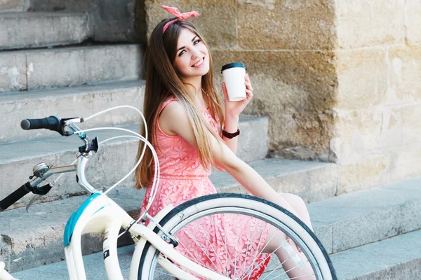 Κορίτσι χαμογελά με ένα φλιτζάνι καφέ και εκλεκτής ποιότητας ποδηλάτων — Φωτογραφία Αρχείου