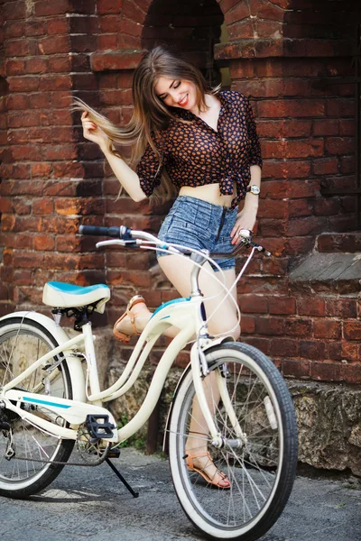 Девушка с велосипедом стоит у стены — стоковое фото