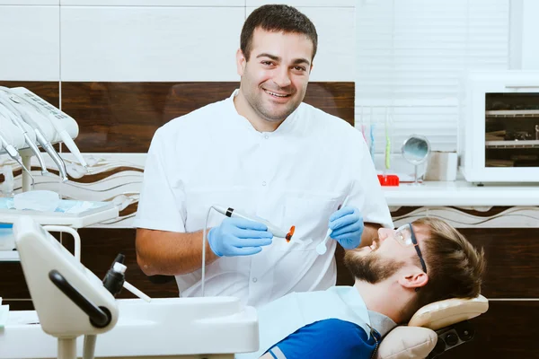 Dentista feliz com lâmpada de fotopolímero e paciente — Fotografia de Stock