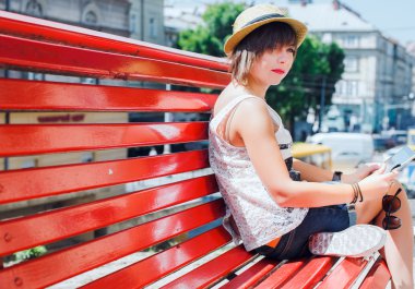dark-blond girl sitting on bench with tablet.