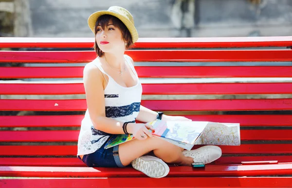 Tourist woman with map of Europe sitting on red bench — стокове фото