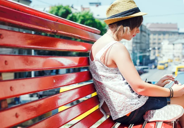 Woman on a red bench, using tablet. — Stockfoto