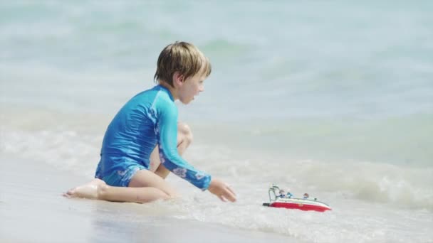 Menino brincando com barco de brinquedo no oceano — Vídeo de Stock