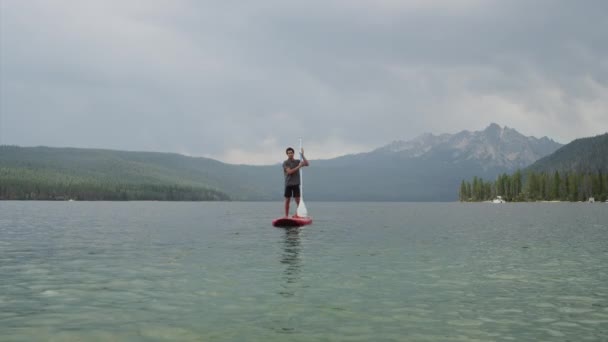 Jonge man paddleboarding op meer — Stockvideo