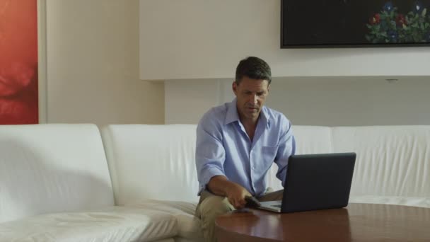 Hombre usando el ordenador portátil y hablando en el teléfono móvil — Vídeo de stock