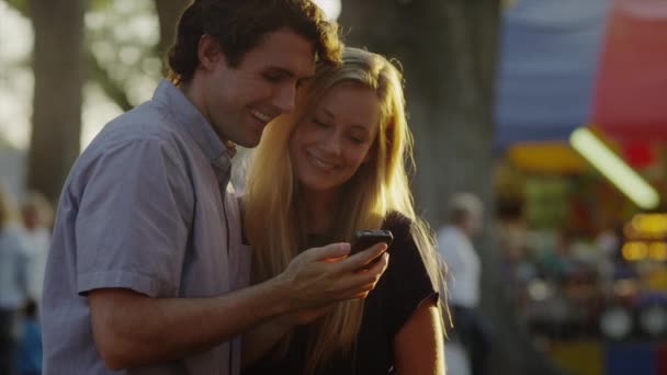 Pareja mirando el teléfono celular en el carnaval — Vídeos de Stock