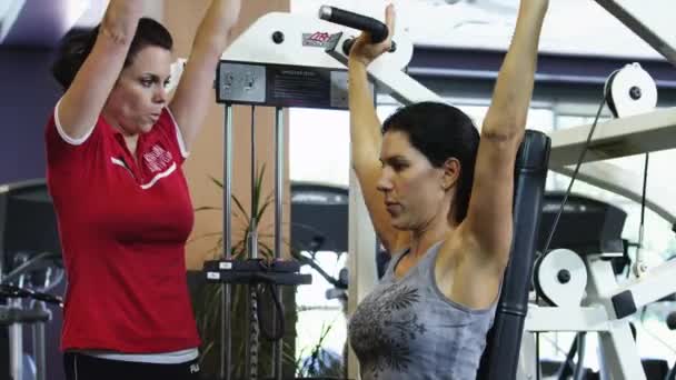 Физический тренер, помогающий женщине в спортзале — стоковое видео