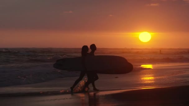 Casal carregando pranchas de surf na praia ao pôr do sol — Vídeo de Stock