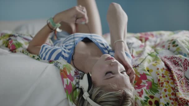 Chica escuchando música con auriculares en la cama — Vídeo de stock