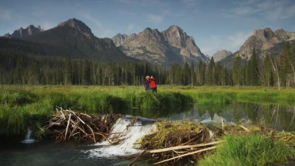 Pareja joven viendo la presa de castor en el lago — Vídeos de Stock